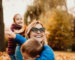 Smiling woman wearing sunglasses hugging children in autumn